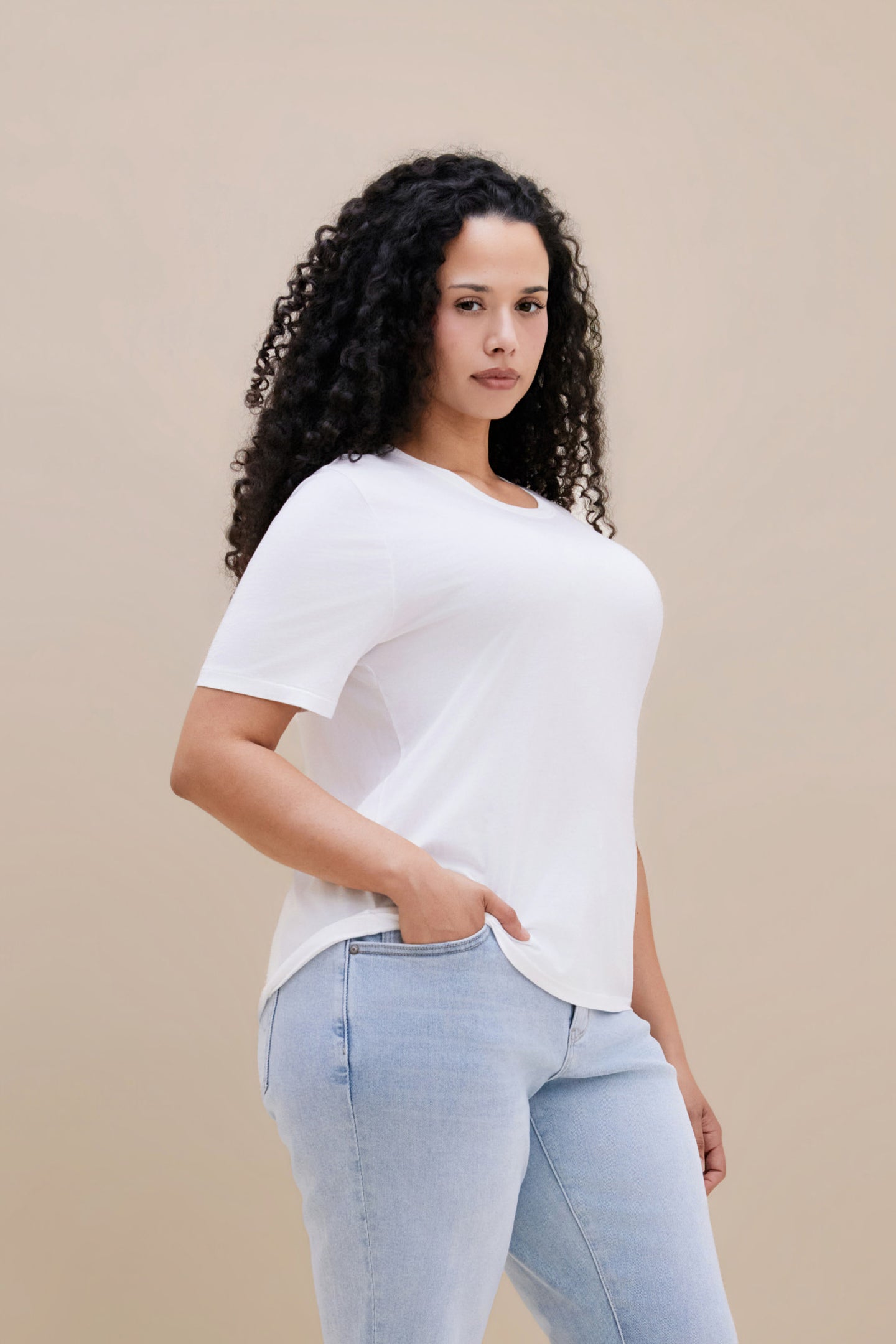 Woman wearing a white t-shirt and light blue jeans against a beige background