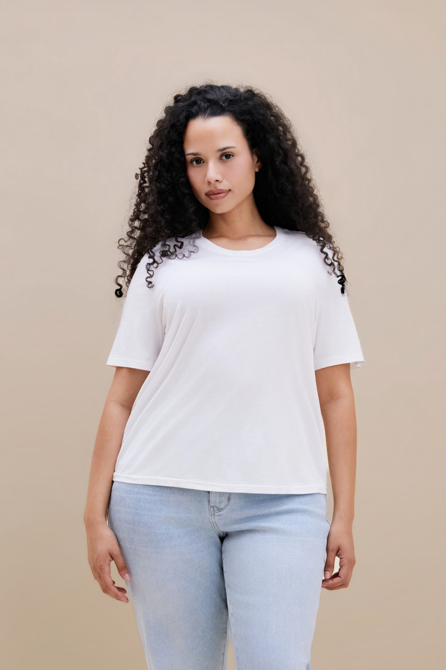 Woman wearing a white t-shirt and light blue jeans against a beige background