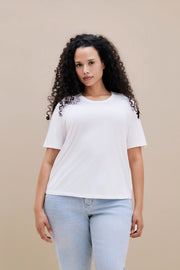 Woman wearing a white t-shirt and light blue jeans against a beige background