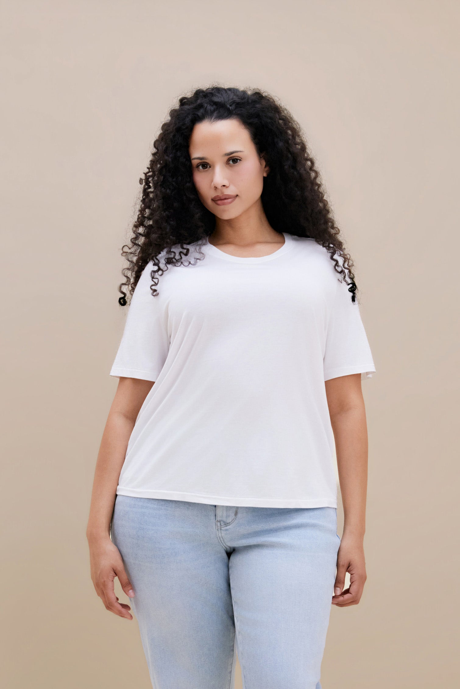 Woman wearing a white t-shirt and light blue jeans against a beige background