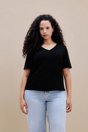 Woman wearing a black t-shirt and light blue jeans against a beige background | model-size: 16
