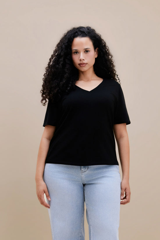 Woman wearing a black t-shirt and light blue jeans against a beige background | model-size: 16