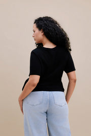Backside of a woman wearing a black t-shirt and light blue jeans against a beige background 