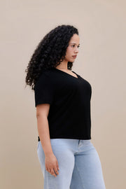 Woman wearing a black t-shirt and light blue jeans against a beige background 