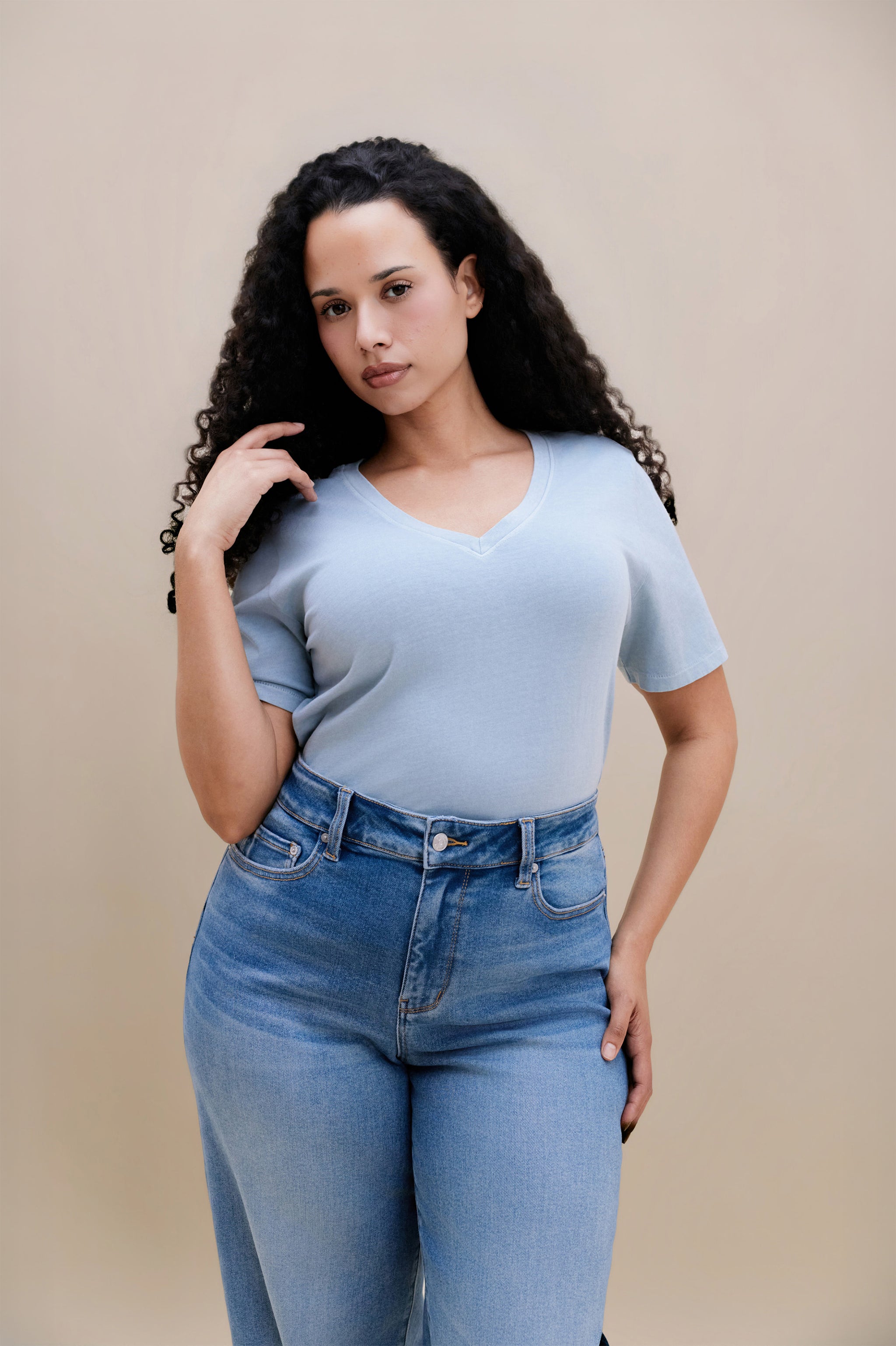 Woman wearing a blue t-shirt and jeans with a beige background  | model-size: 16