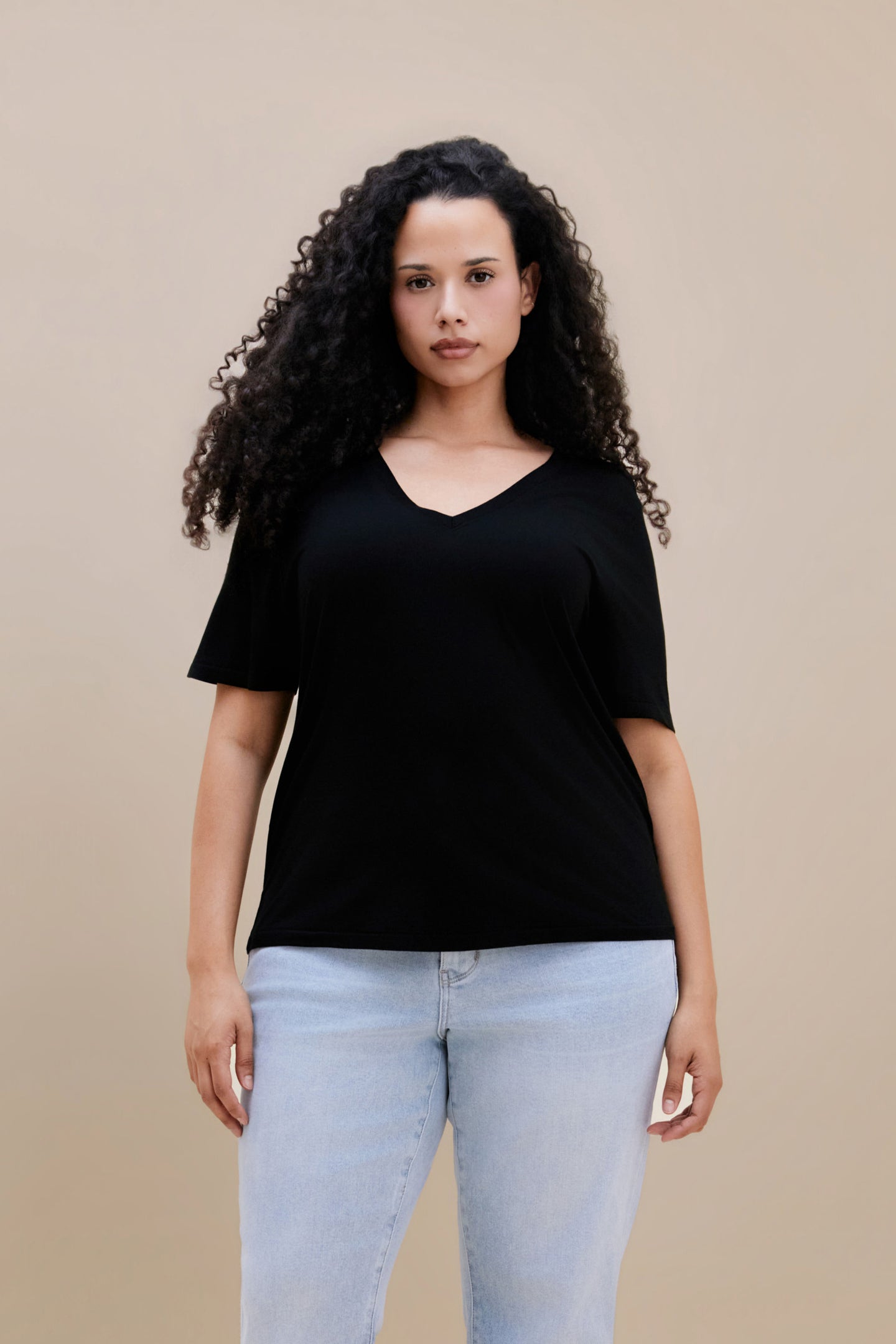 Woman wearing a black t-shirt and light blue jeans against a beige background | model-size: 16