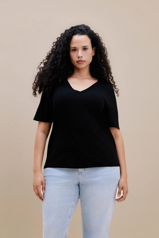 Woman wearing a black t-shirt and light blue jeans against a beige background | model-size: 16