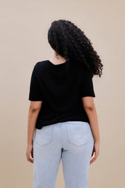 Backside of a woman wearing a black t-shirt and light blue jeans against a beige background