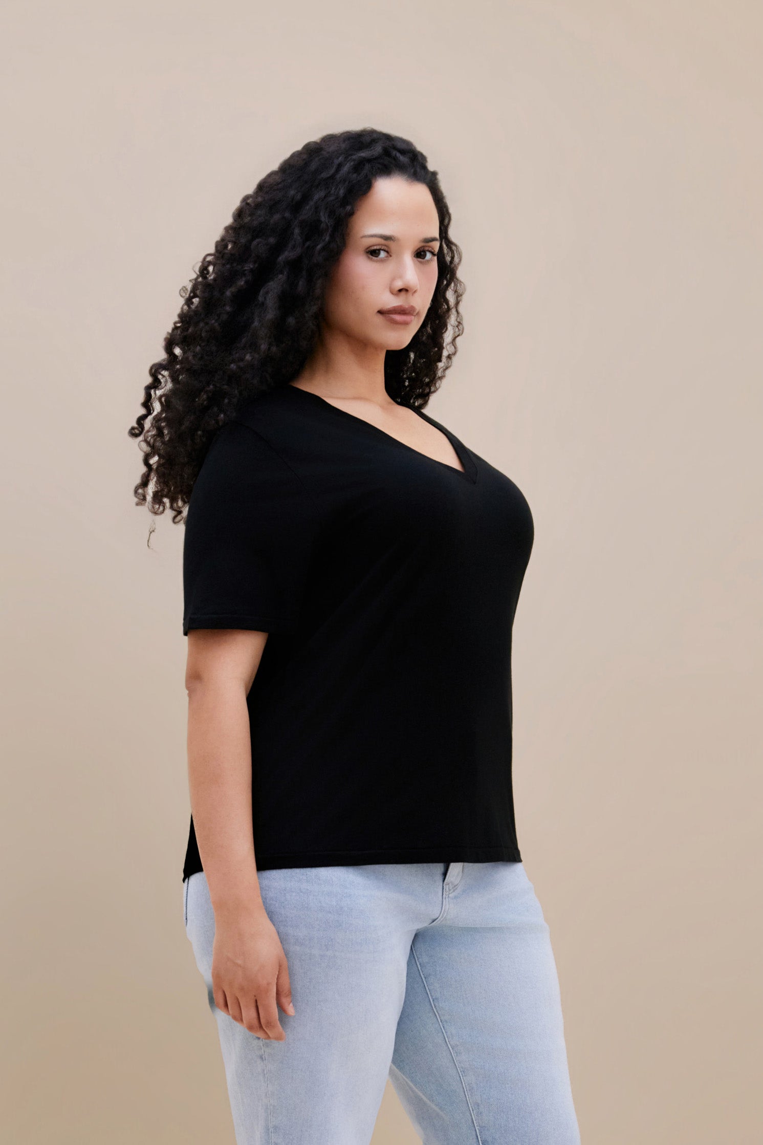 Woman wearing a black t-shirt and light blue jeans against a beige background
