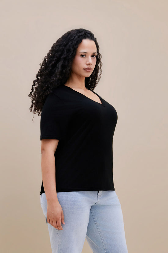 Woman wearing a black t-shirt and light blue jeans against a beige background