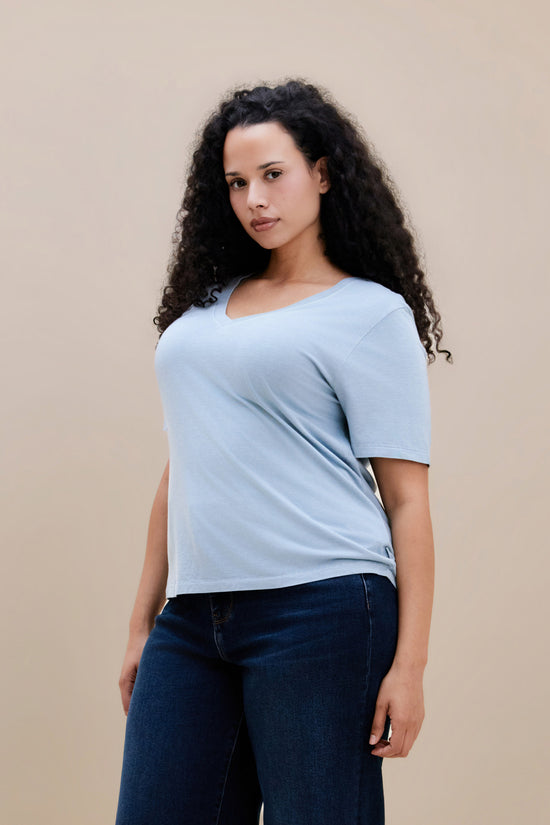 Woman wearing a light blue t-shirt and dark jeans against a beige background