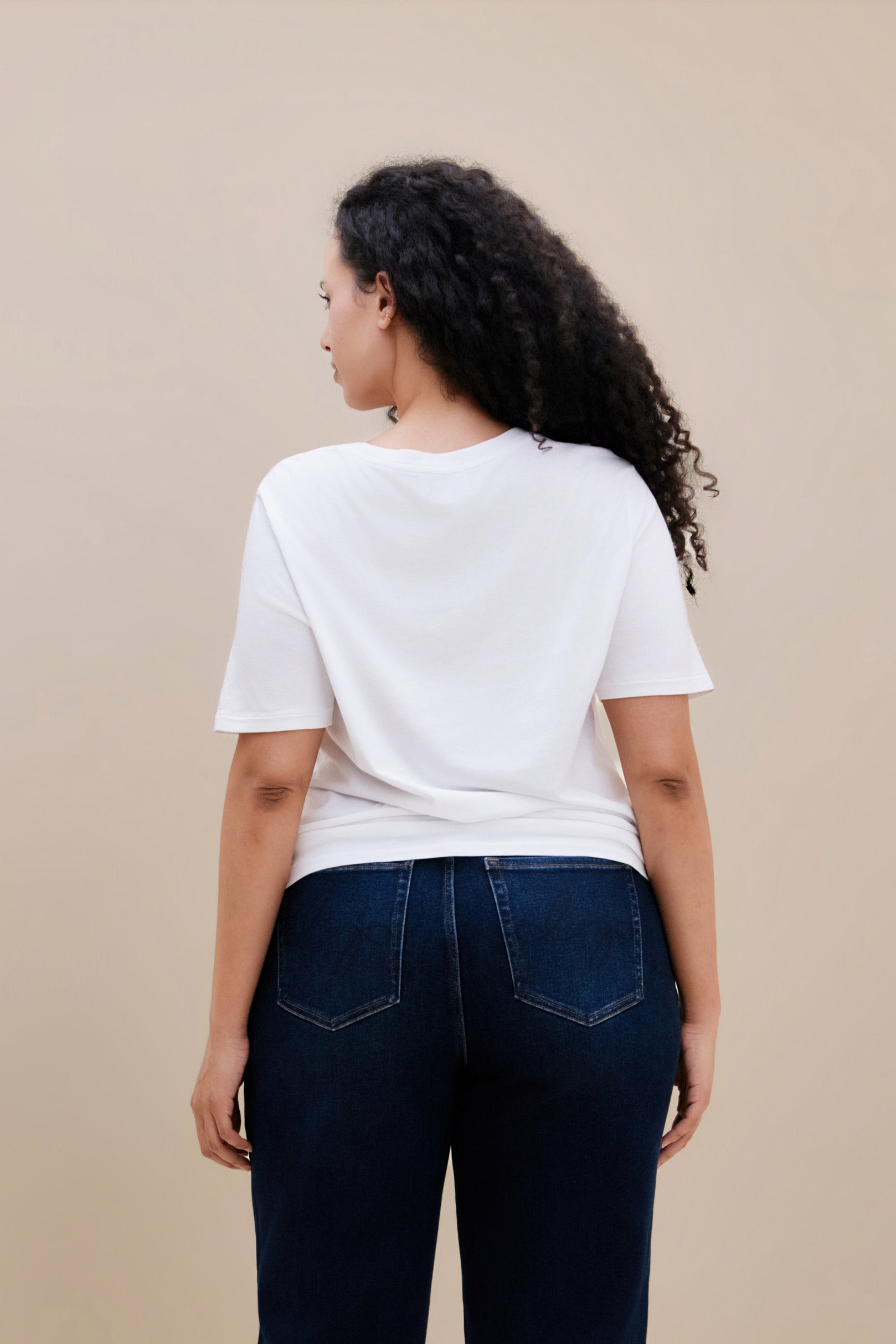 Woman wearing a plain white t-shirt and dark jeans against a beige background