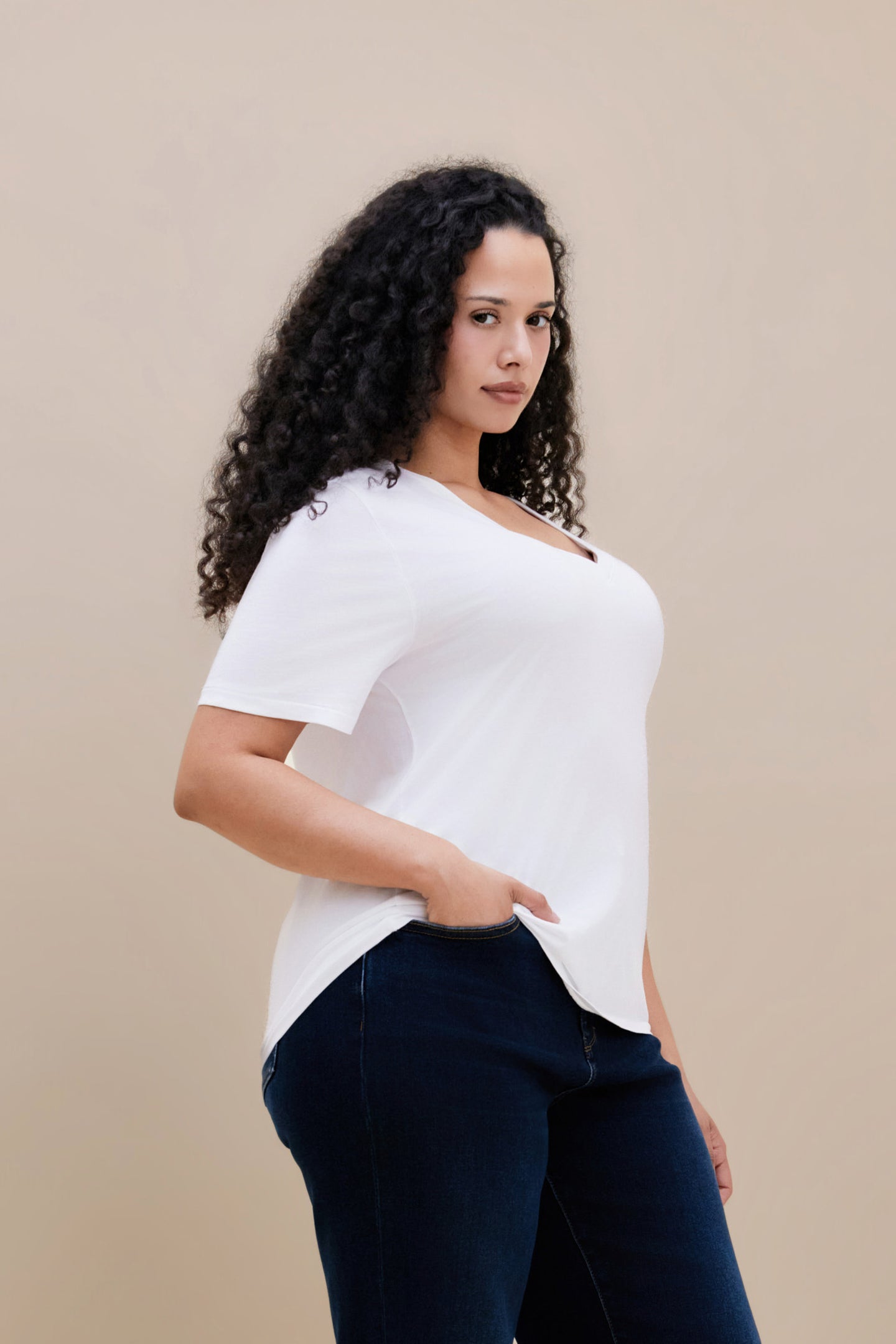 Woman wearing a plain white t-shirt and dark jeans against a beige background
