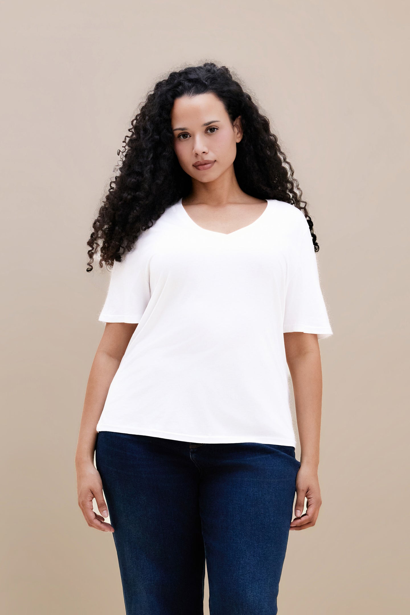 Woman wearing a plain white t-shirt and dark jeans against a beige background | model-size: 16