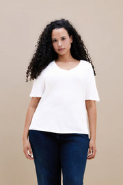 Woman wearing a plain white t-shirt and dark jeans against a beige background | model-size: 16