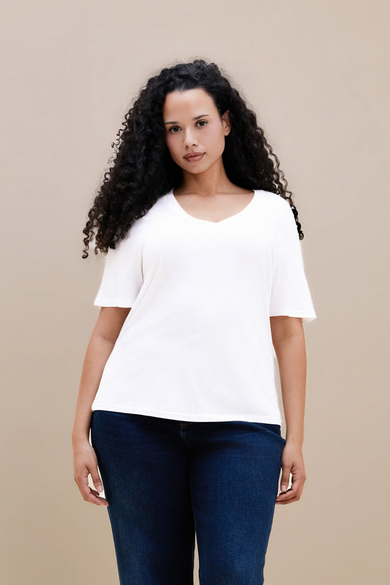 Woman wearing a plain white t-shirt and dark jeans against a beige background | model-size: 16