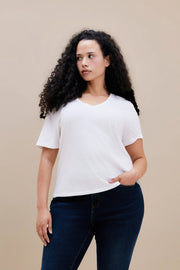 Woman wearing a plain white t-shirt and dark jeans against a beige background
