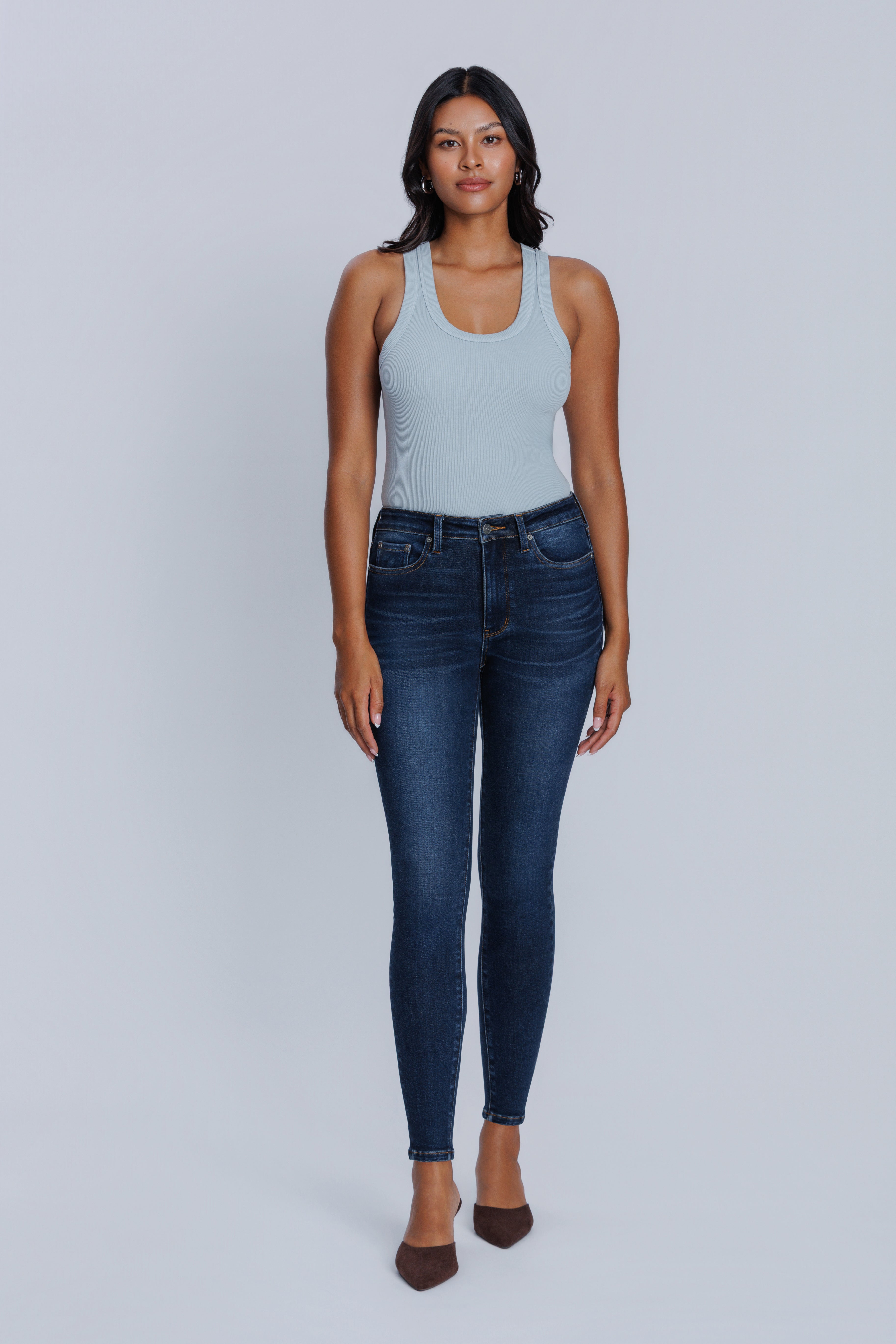 Woman wearing a DePart light blue tank top and dark blue jeans on a gray background
