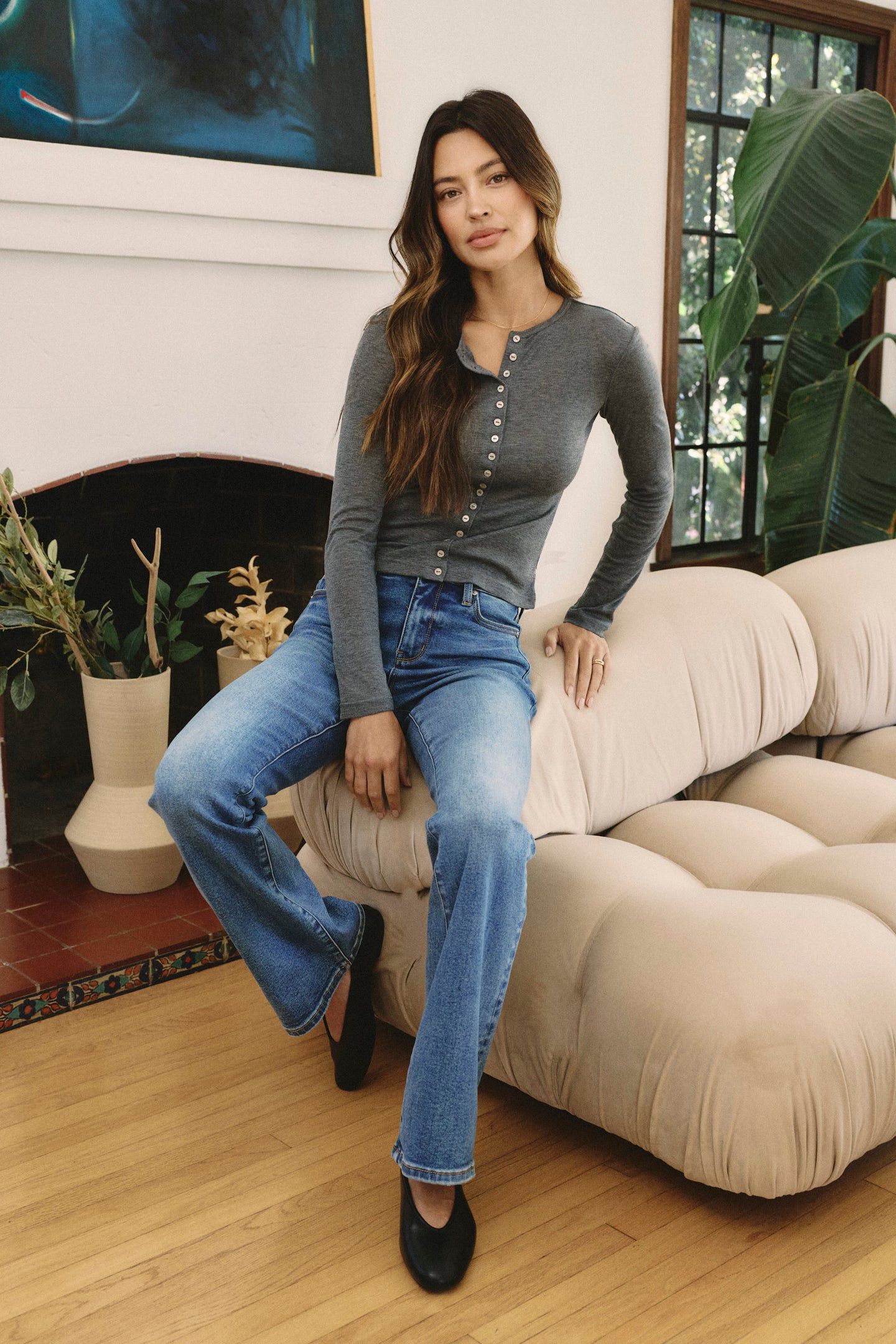 Woman sitting on a beige sofa in a living room with plants and a fireplace | model-size: 4
