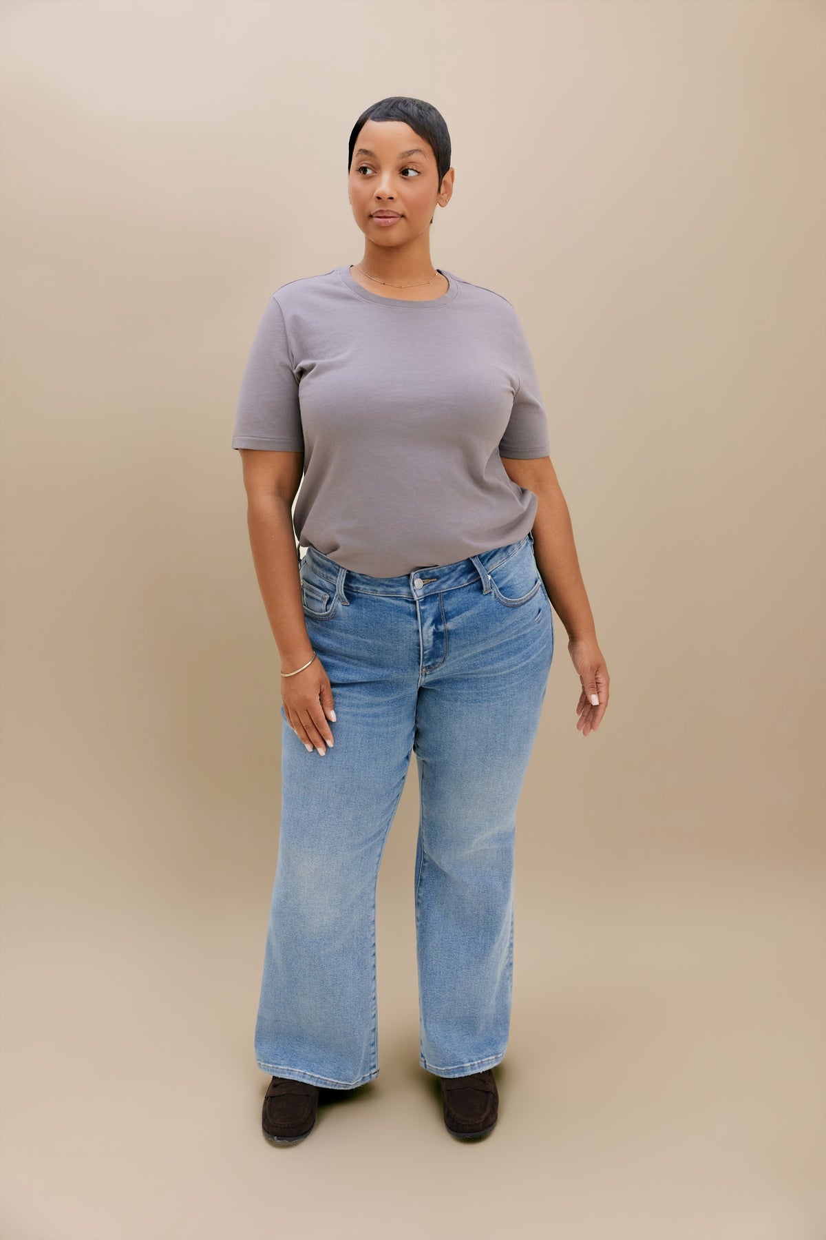 A woman modeling a light gray short-sleeve t-shirt and light blue wide-leg jeans against a solid beige studio background.