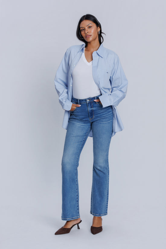 Woman wearing a light blue shirt, DePart white top, and blue jeans on a plain background
