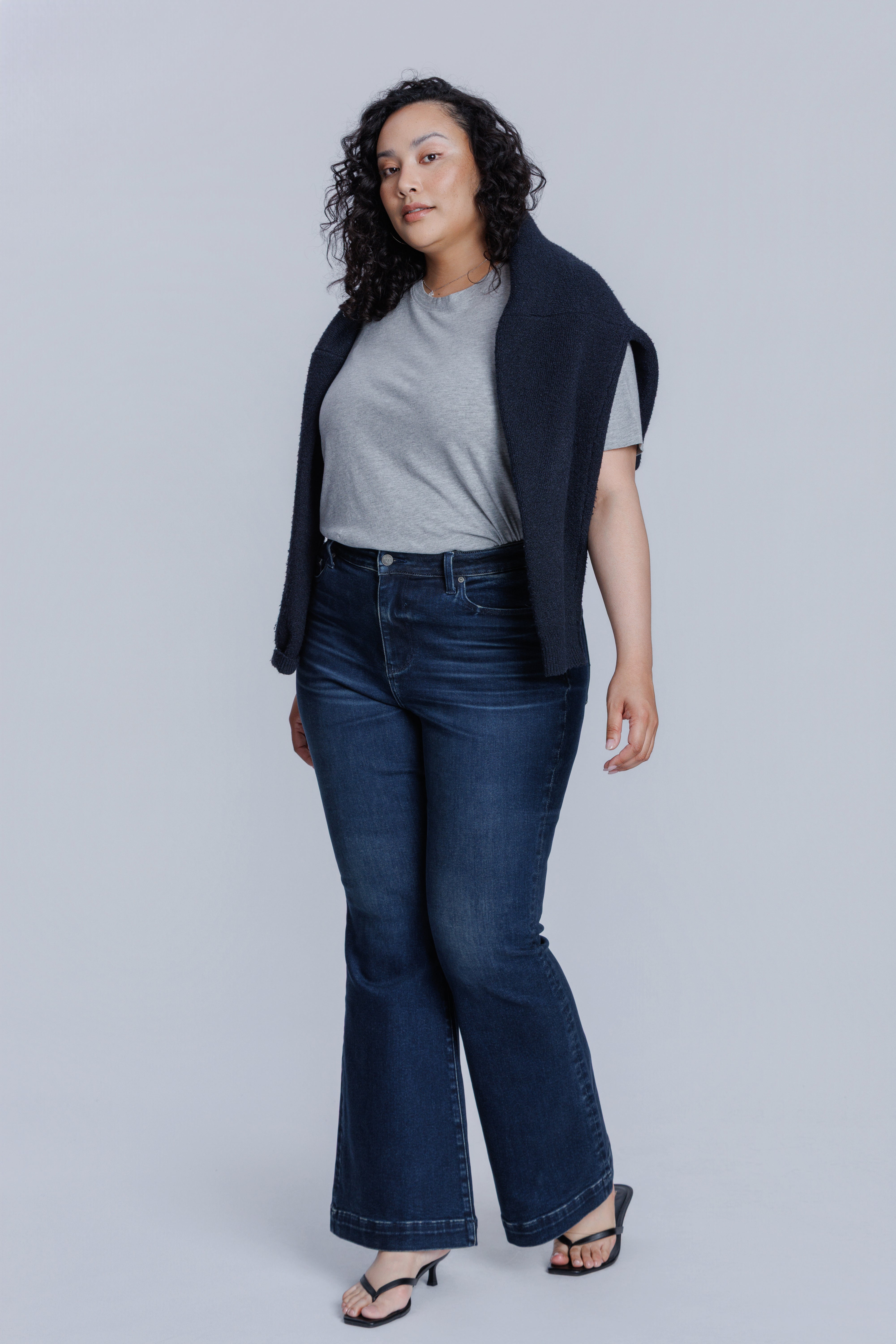 Woman wearing a DePart gray t-shirt and dark blue jeans on a light gray background