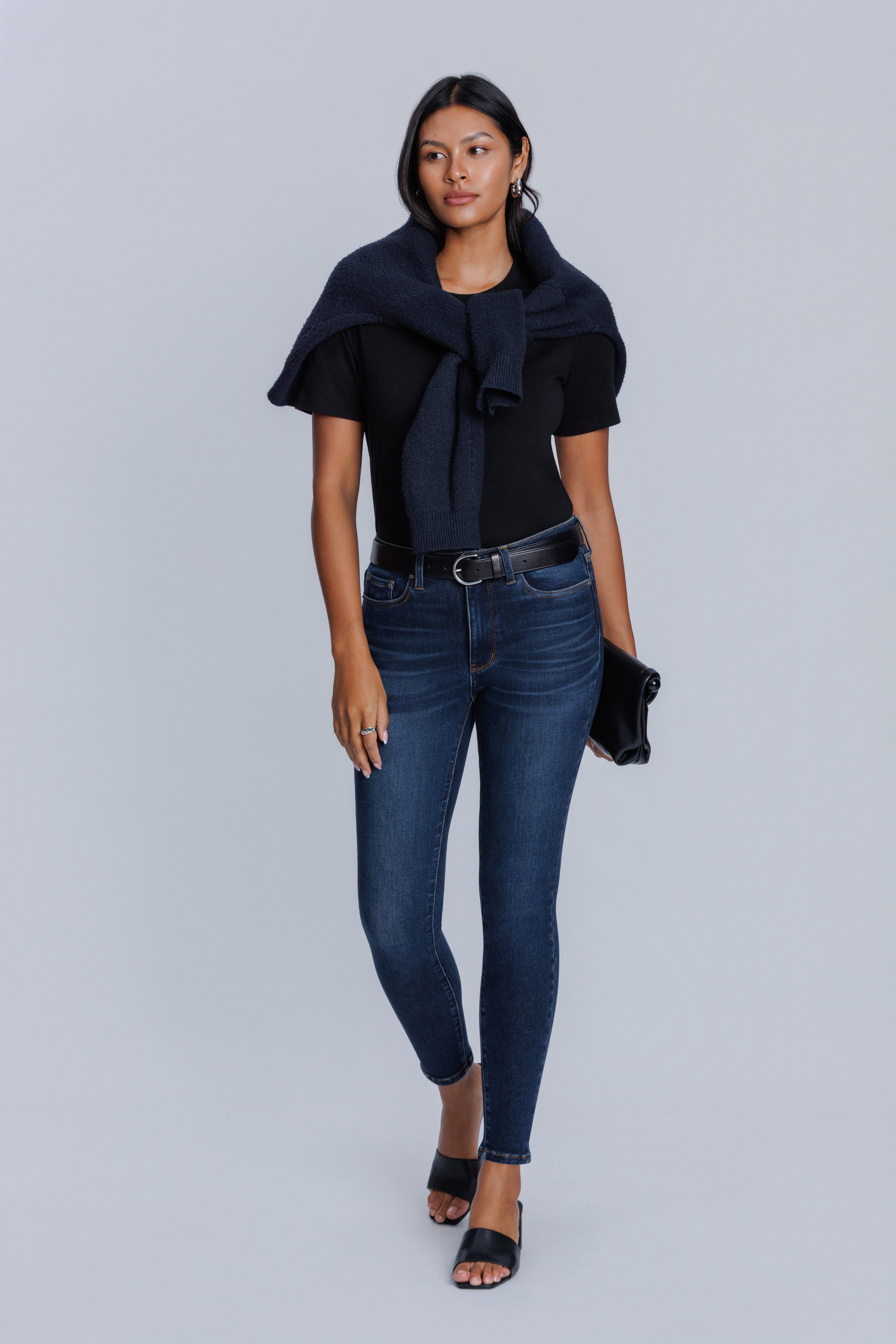 Woman wearing a DePart black top and blue jeans on a gray background