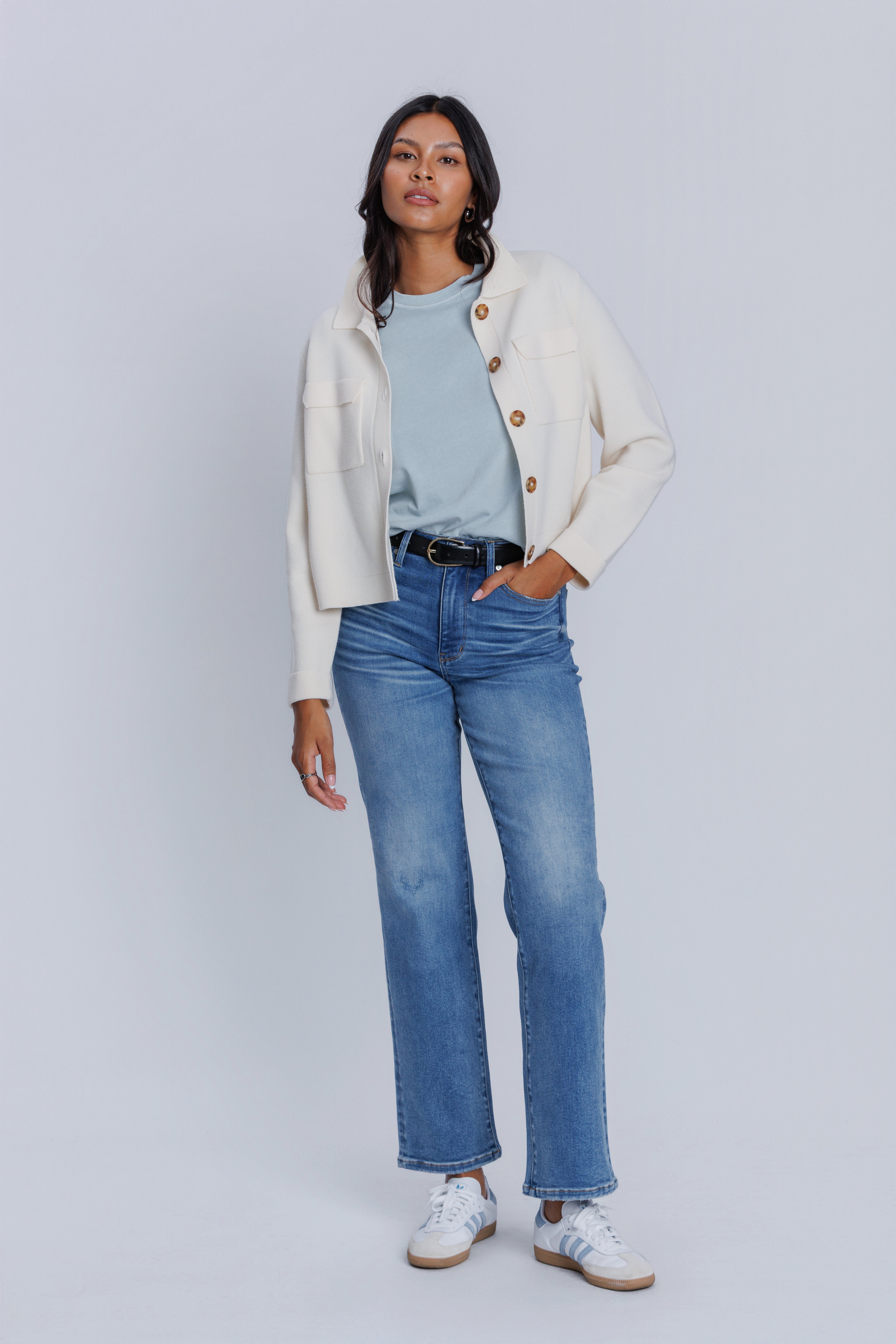 Woman wearing a cream cardigan, DePart light blue shirt, and jeans on a white background