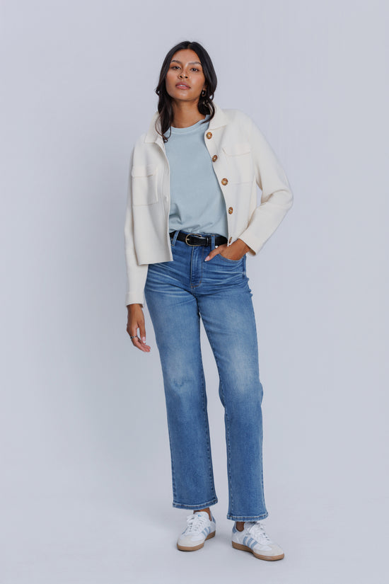 Woman wearing a cream cardigan, DePart light blue shirt, and jeans on a white background