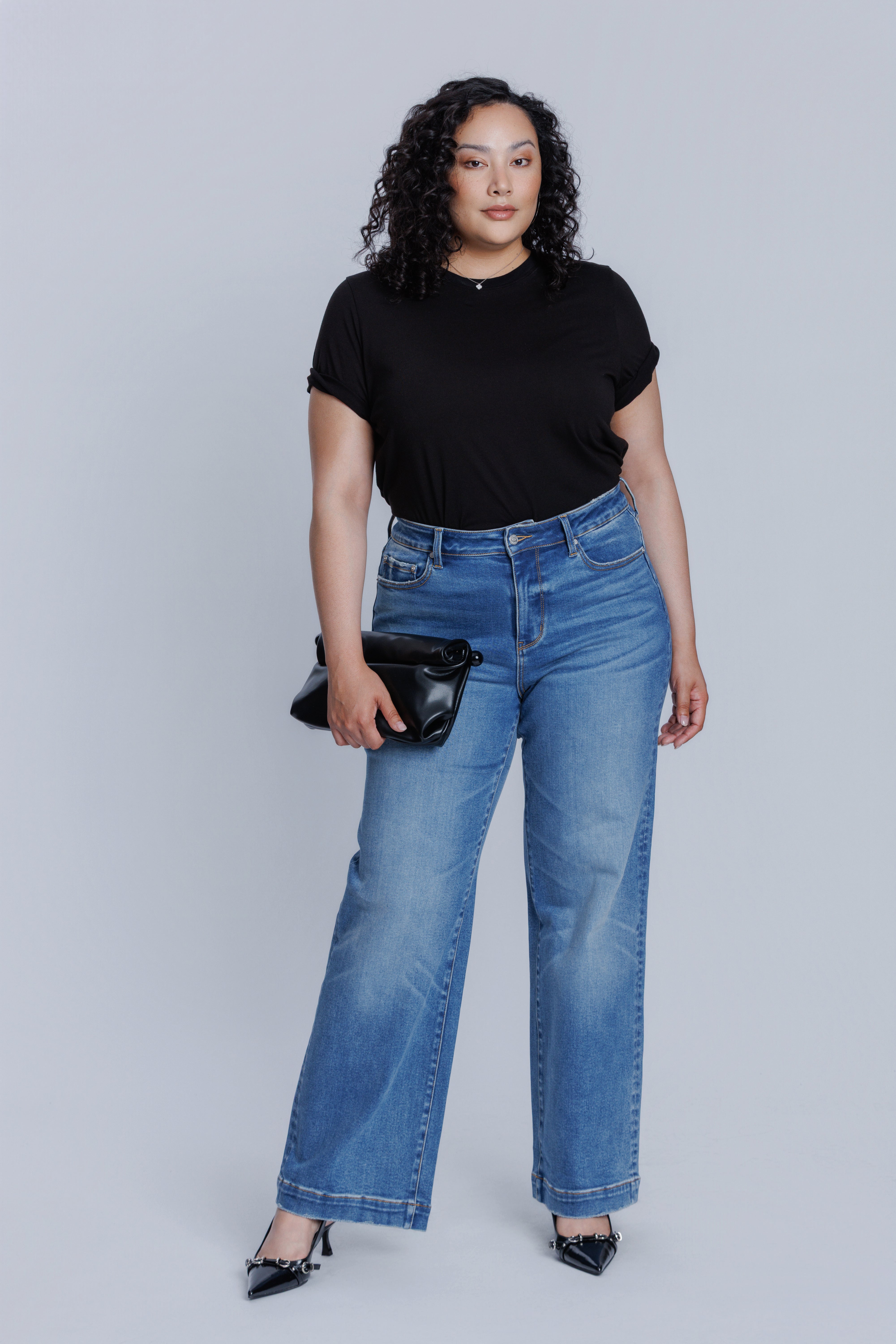 Woman wearing a DePart black t-shirt and blue jeans against a white background