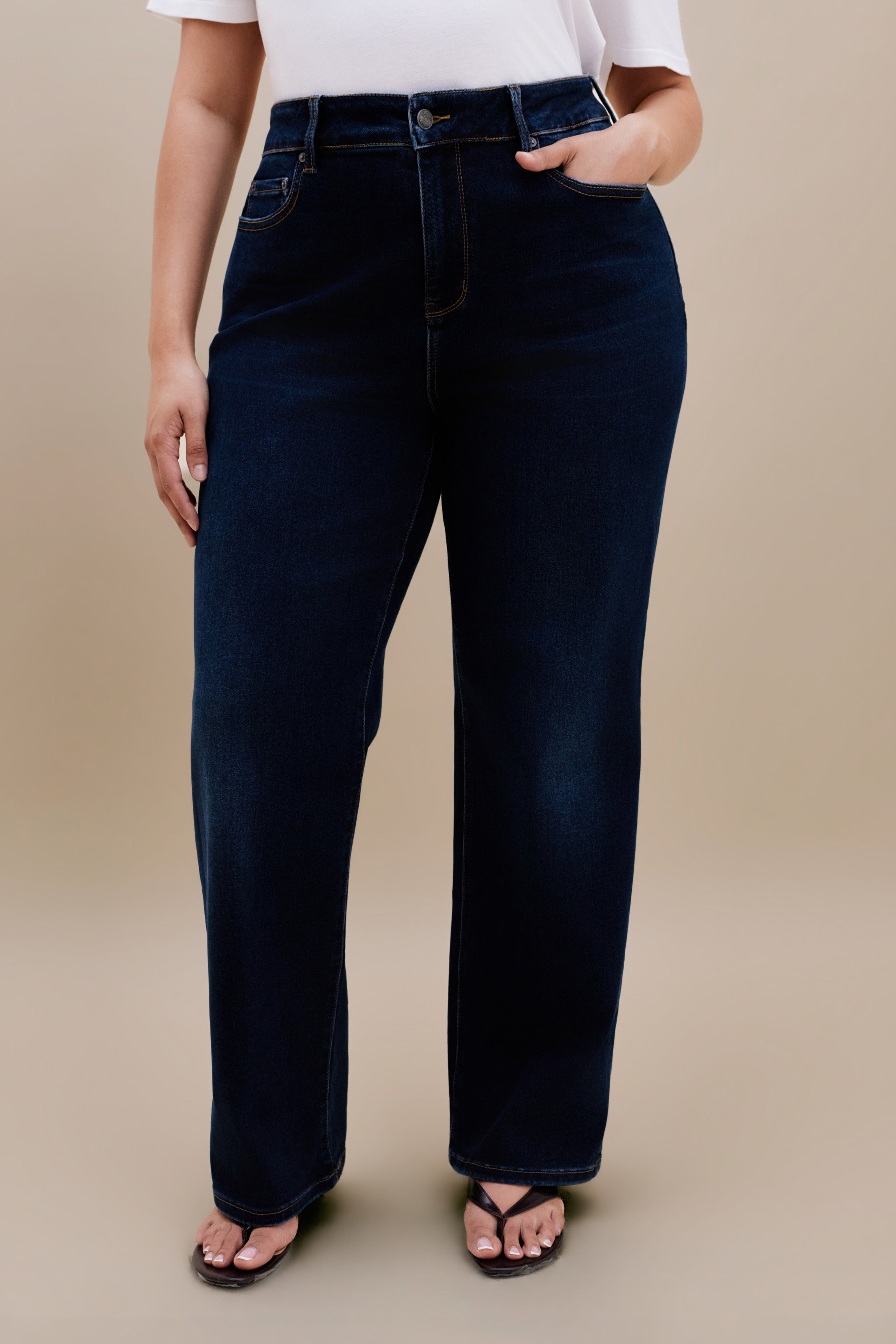 Bottom close up of dark straight jeans against a beige background
