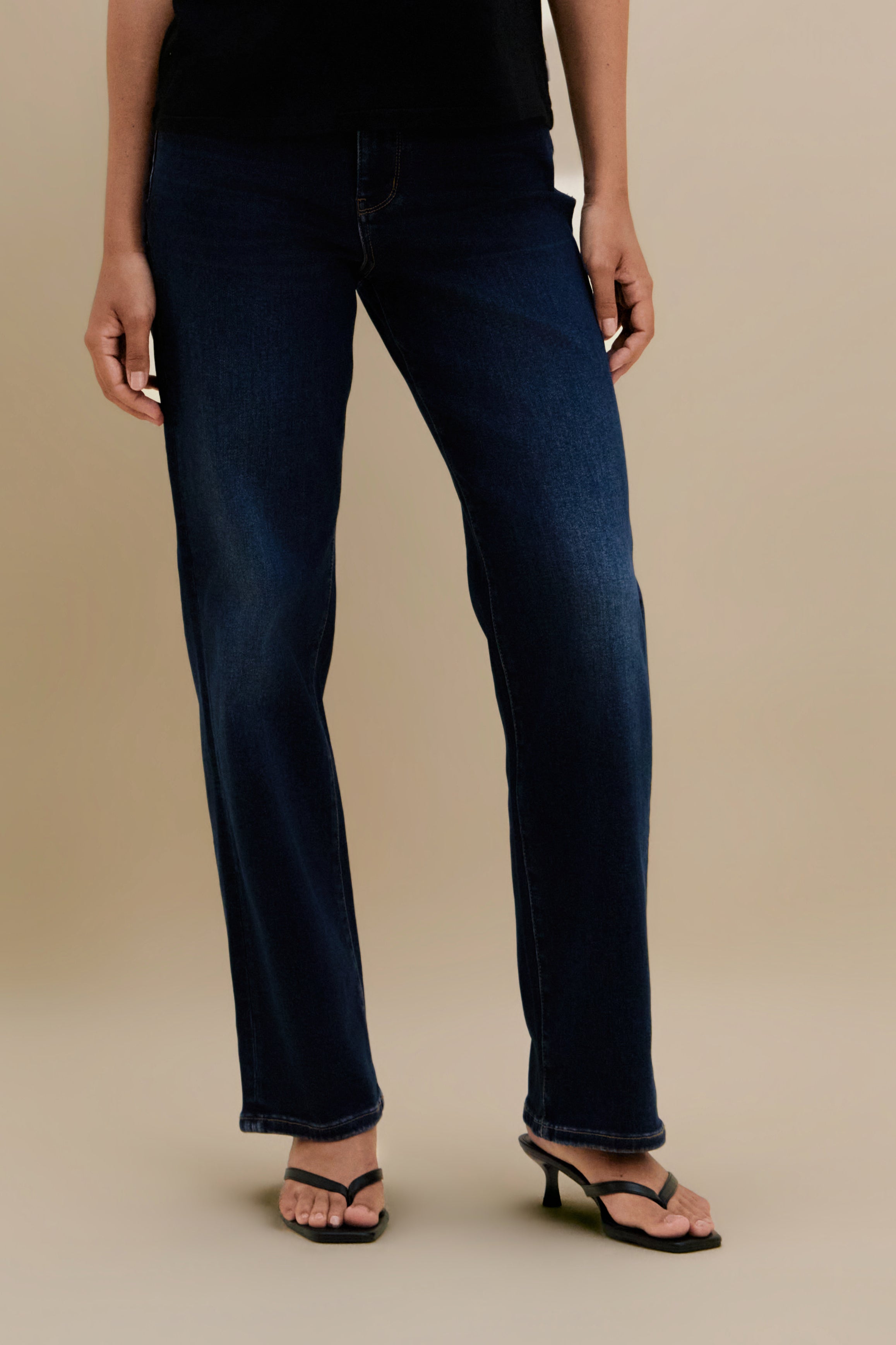 Bottom close up of dark straight jeans against a beige background