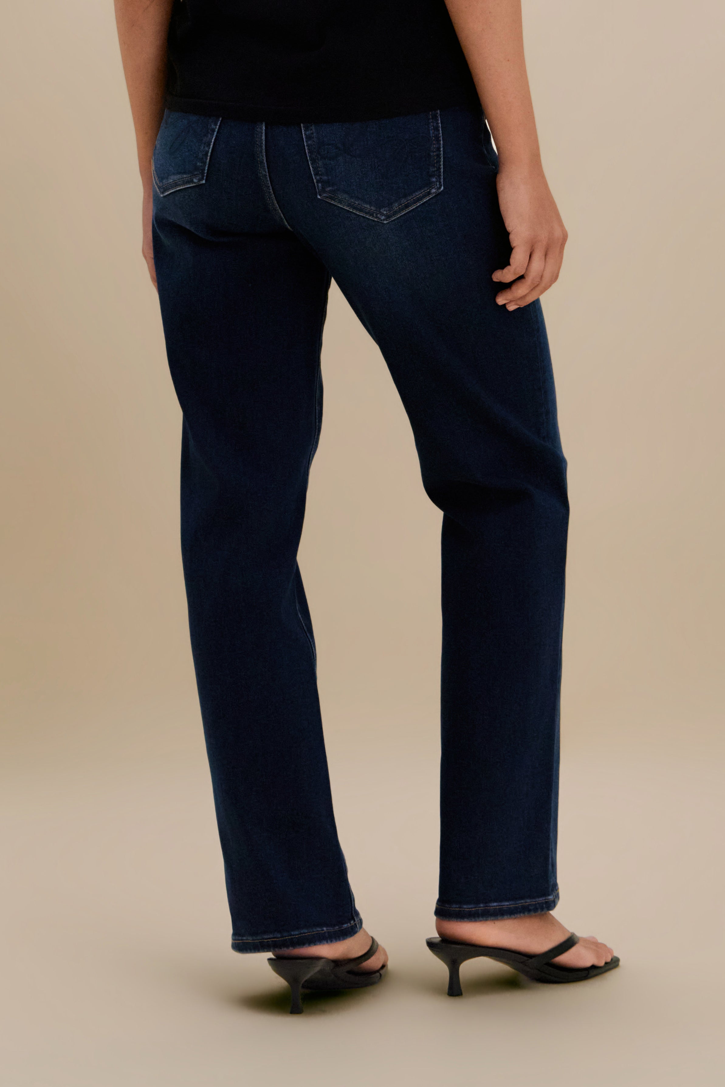 Bottom close up, backside, of dark straight jeans against a beige background