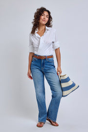 Woman wearing a white shirt and blue jeans, holding a striped bag on a light gray background | model-size: 4