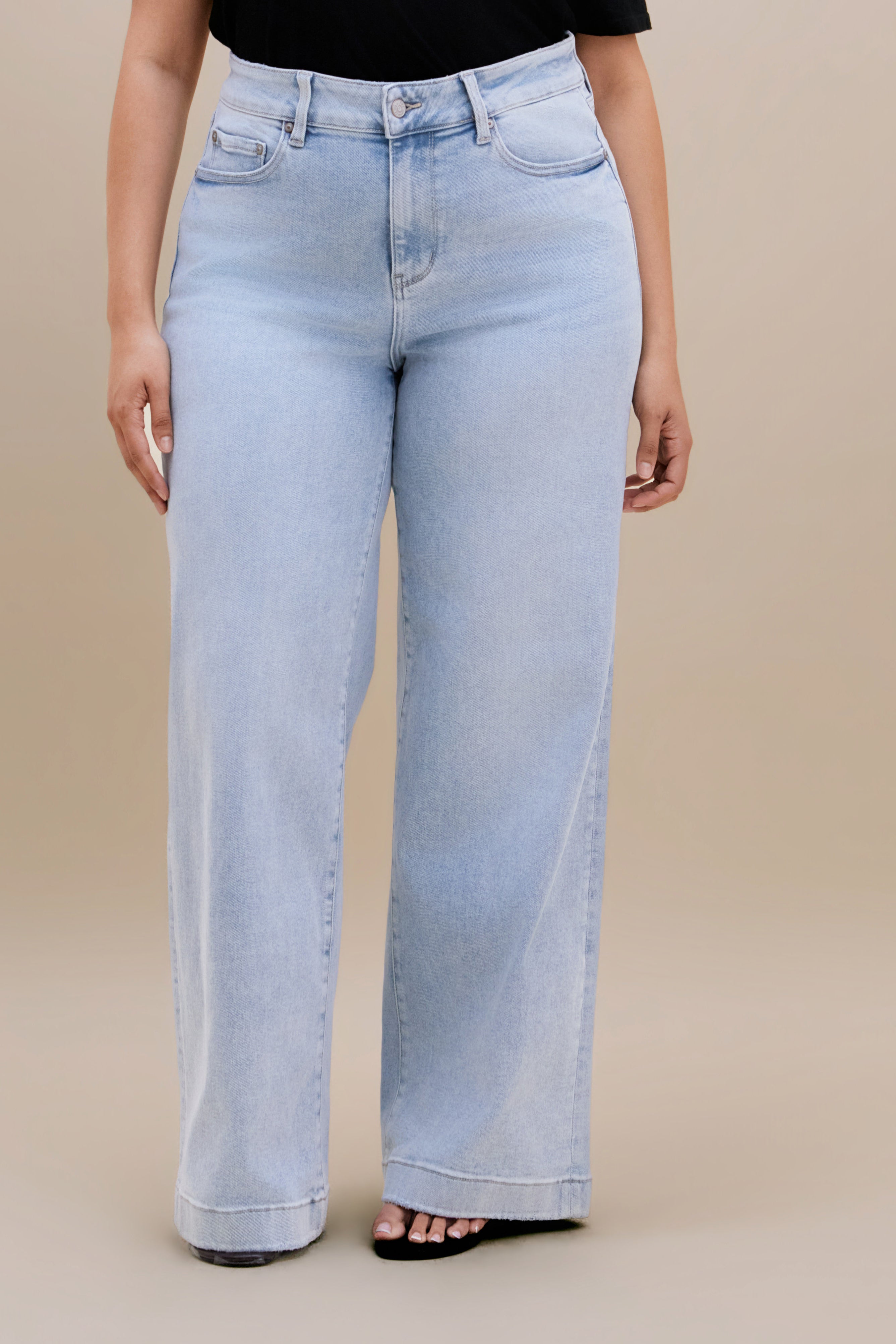 Bottom close up of light wide leg jeans against a beige background