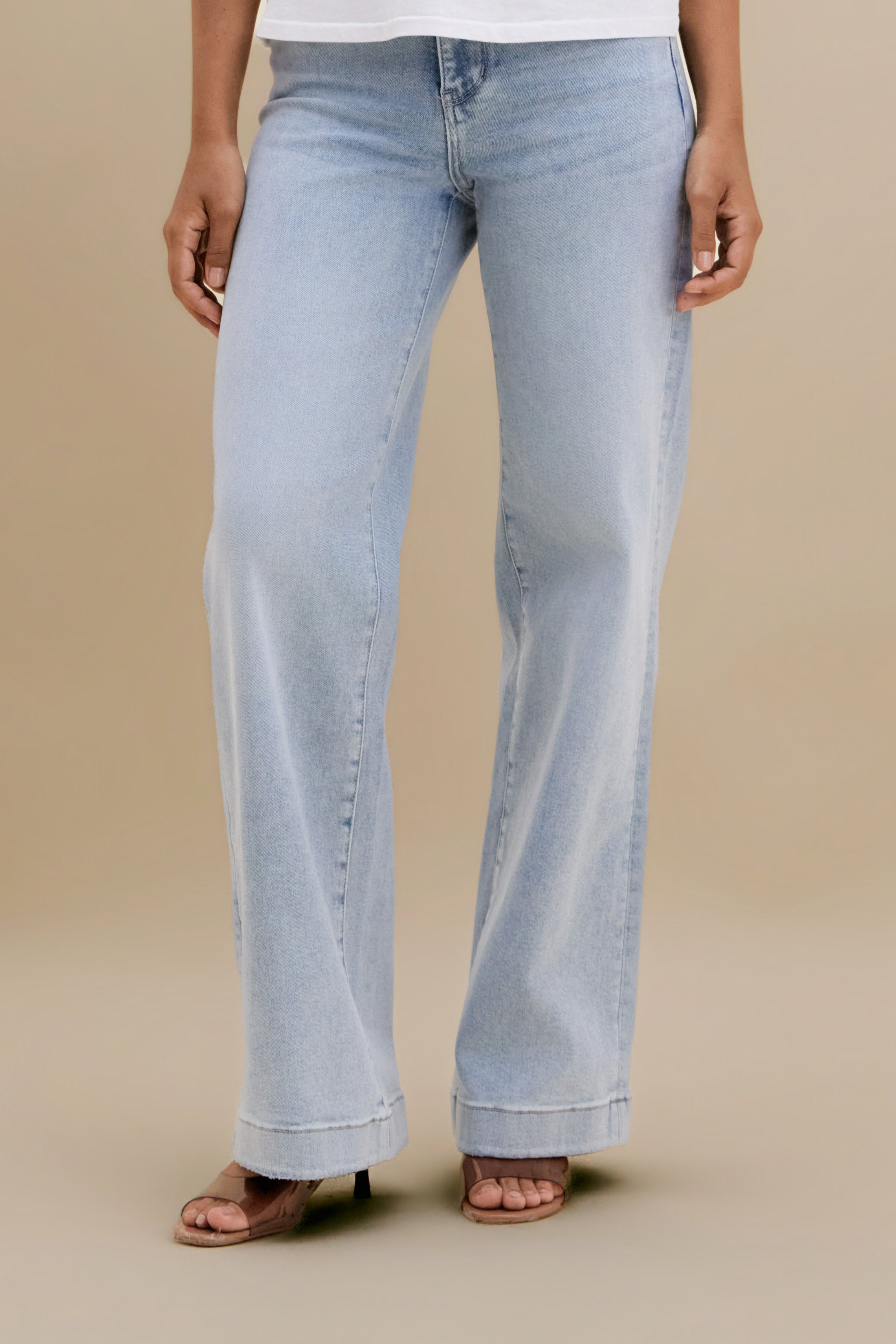 Bottom close up of light wide leg jeans against a beige background