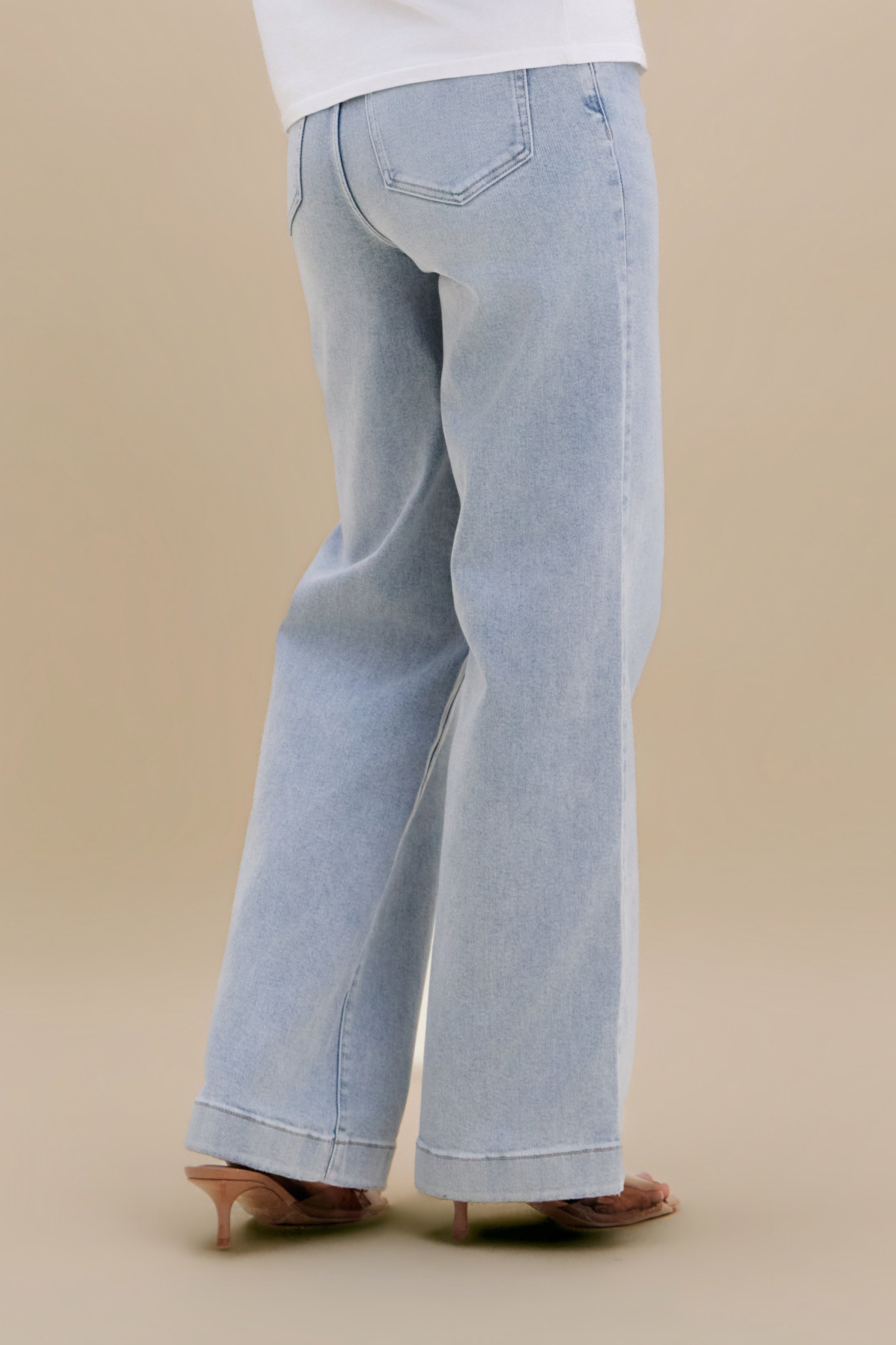 Bottom close up, backside, of light wide leg jeans against a beige background