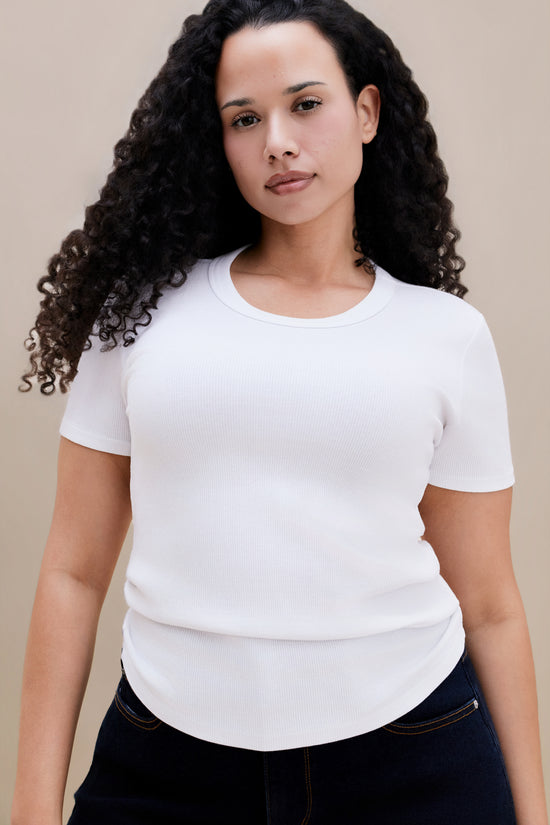 Person wearing a plain white t-shirt and dark jeans on a beige background 