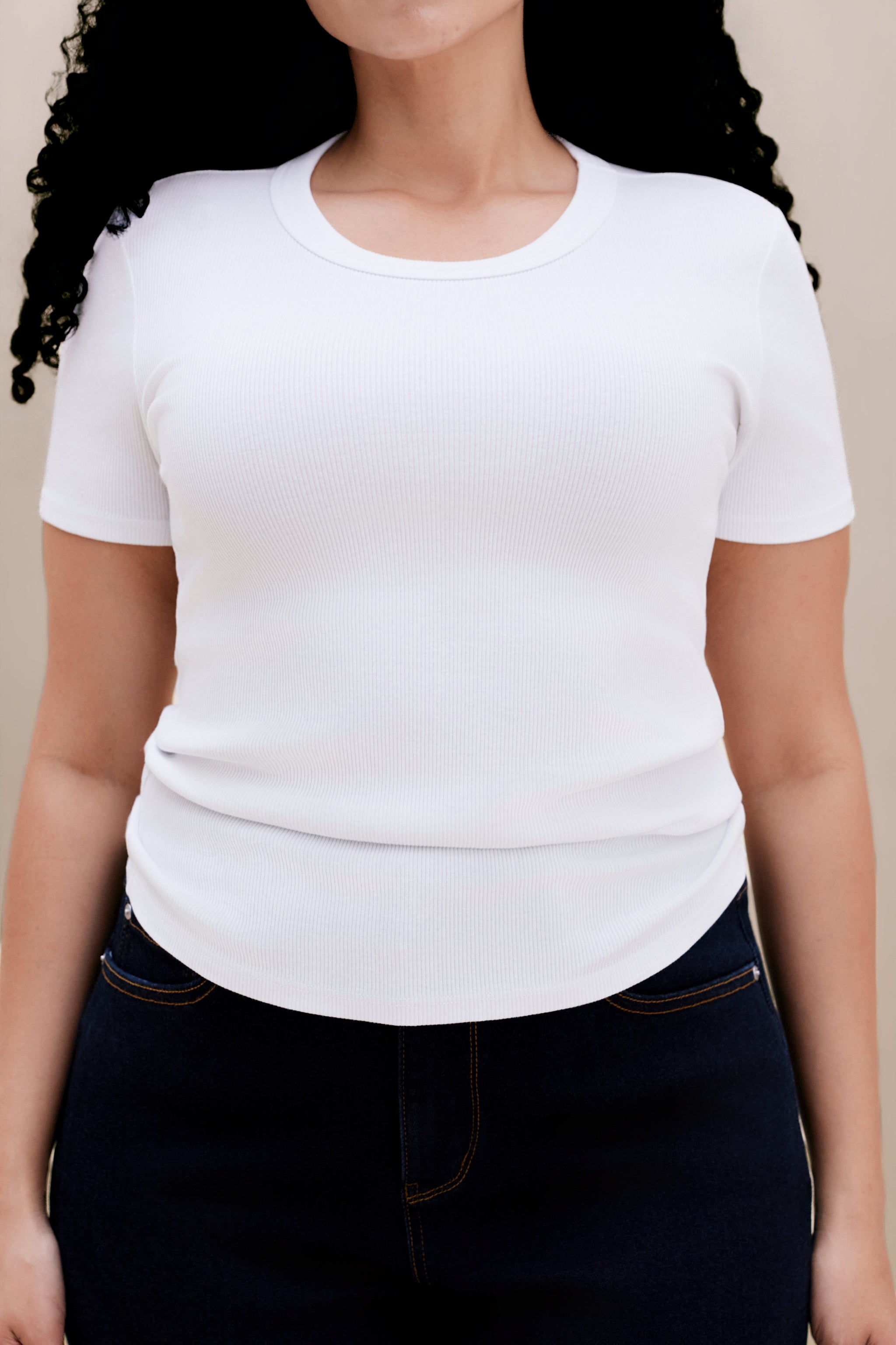 Person wearing a plain white t-shirt and dark jeans on a beige background