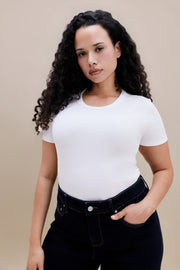 Person wearing a plain white t-shirt and dark jeans on a beige background | model-size: 16