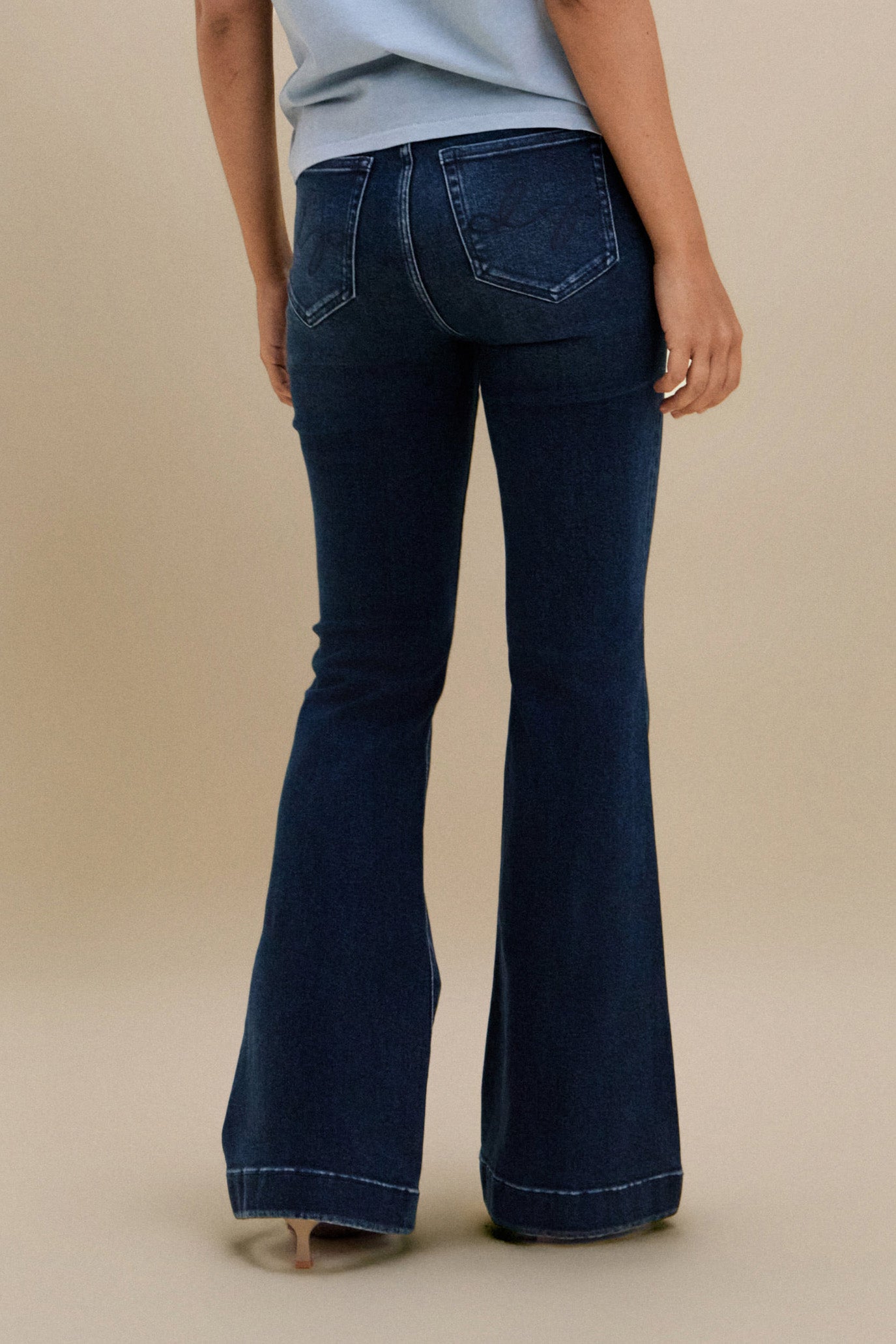 Bottom close up, backside, of dark flare jeans against a beige background