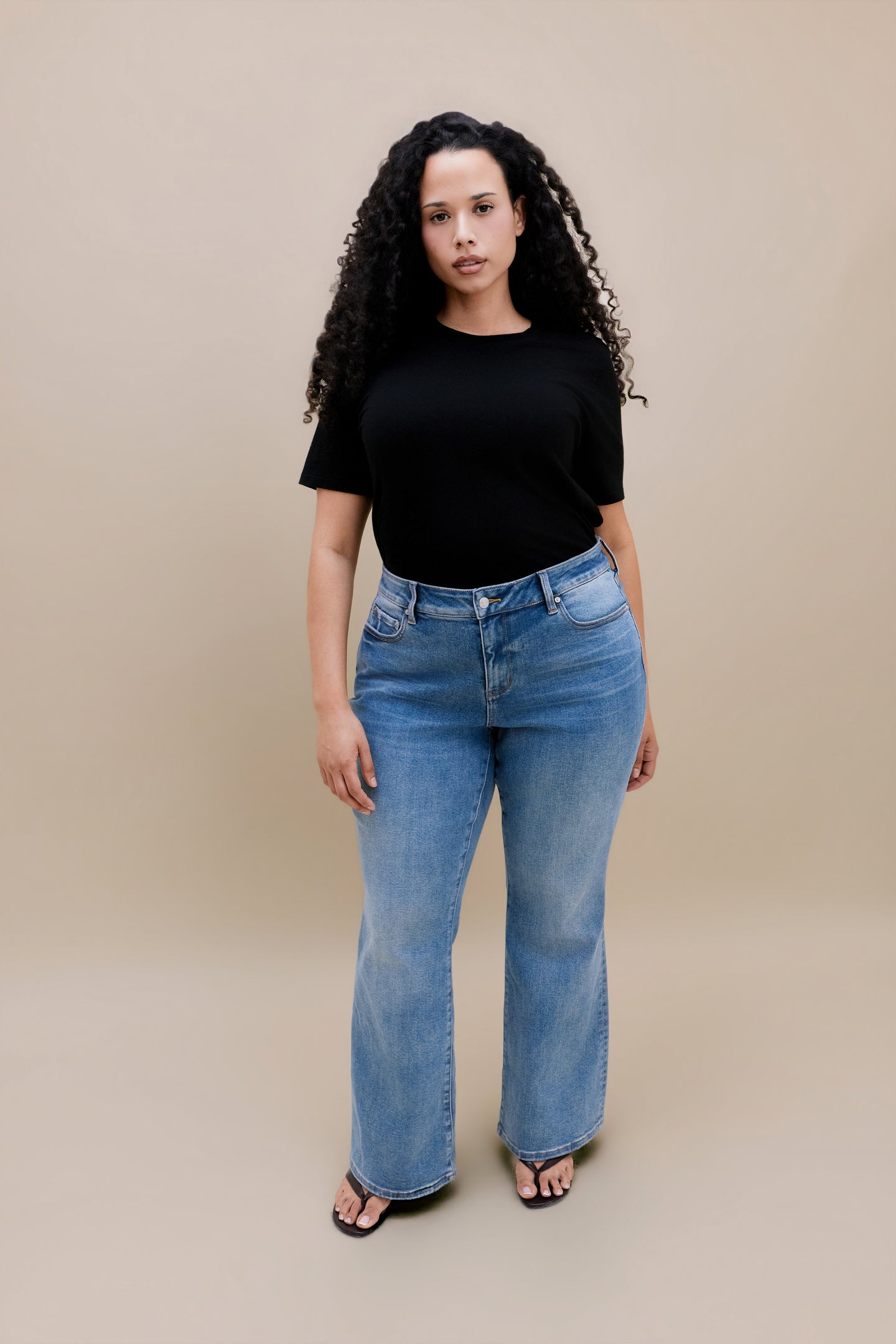 Woman wearing black t-shirt and bootcut jeans with a beige background | model size: 16