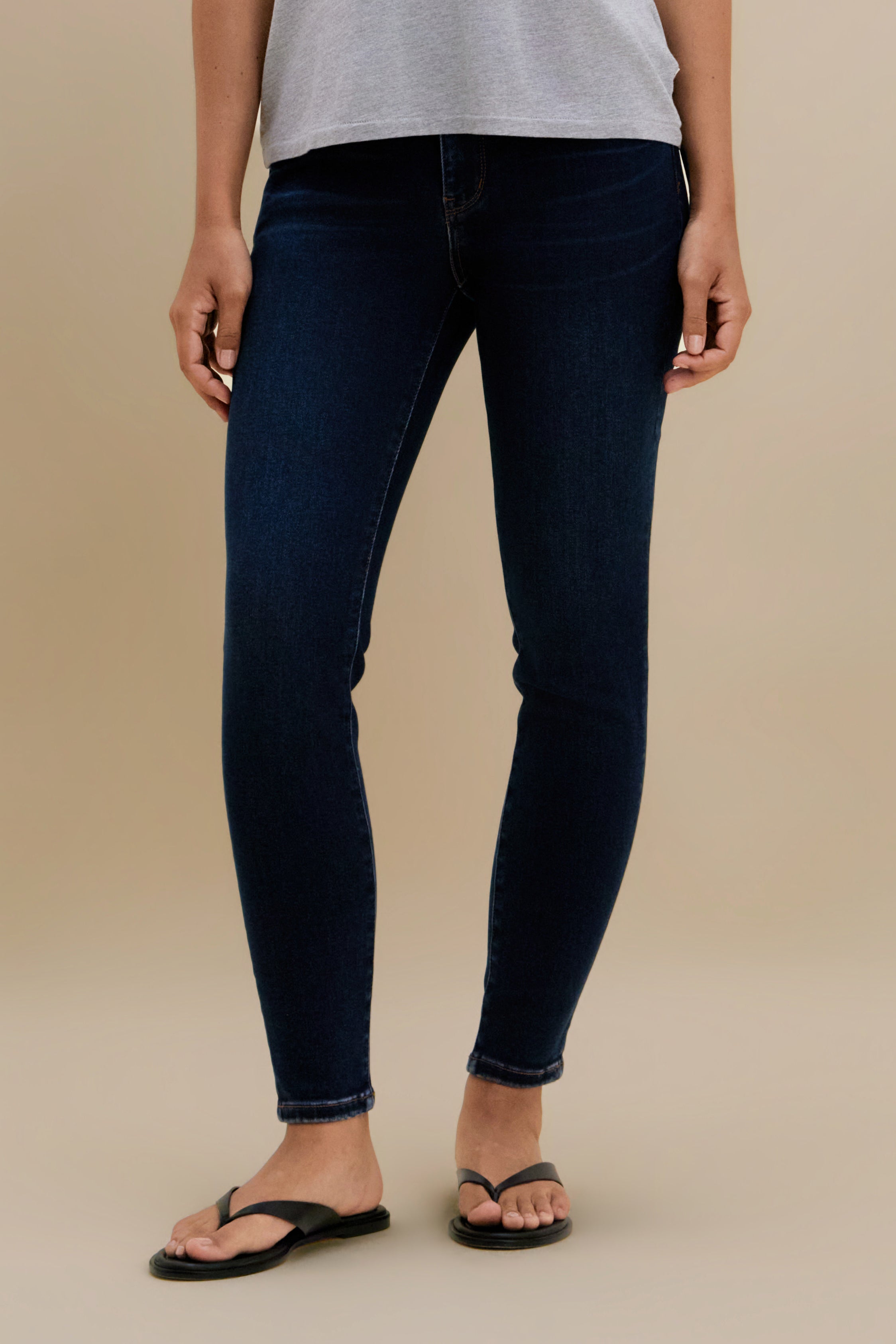 Bottom close up of dark skinny jeans against a beige background