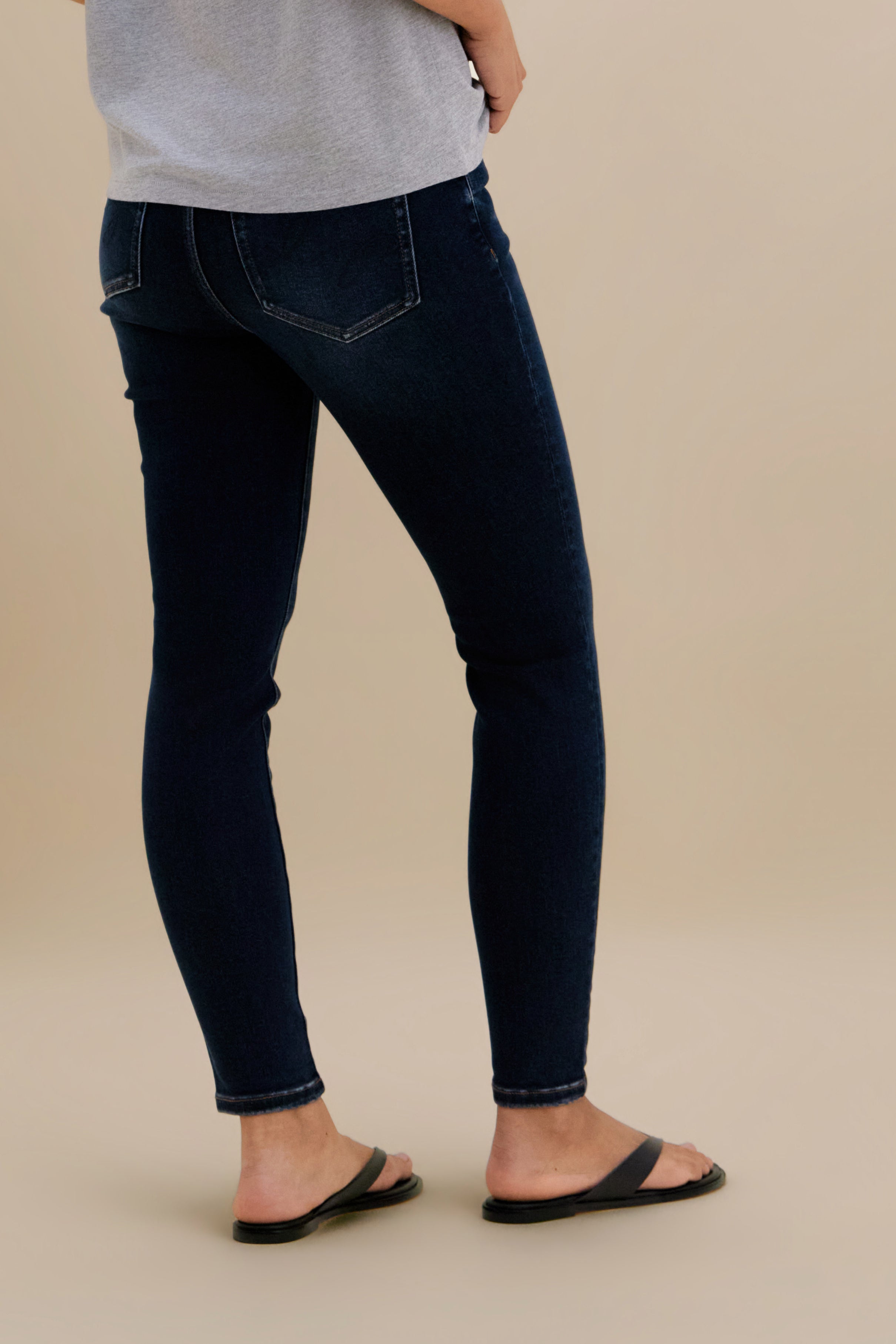 Bottom close up, backside, of dark skinny jeans against a beige background