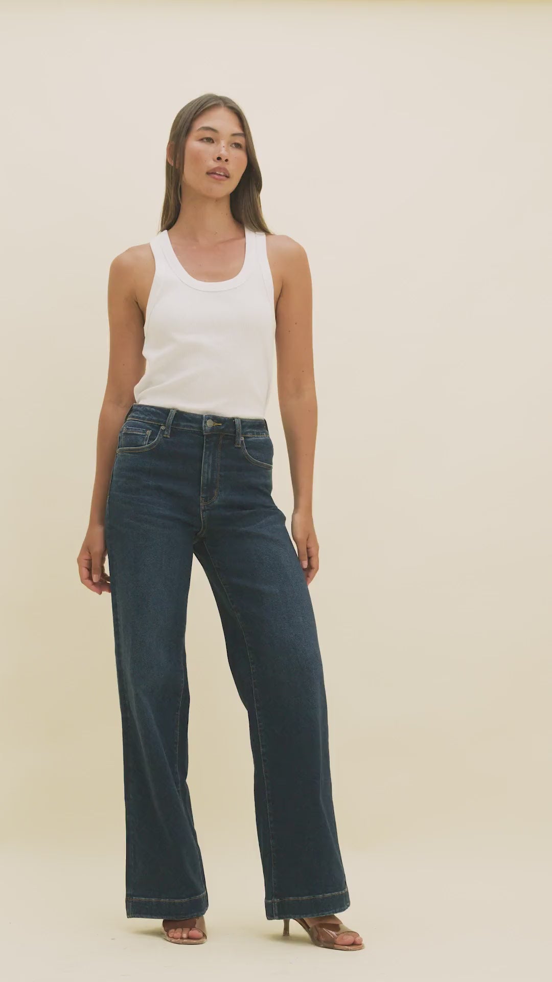 Video of a woman wearing dark wide-leg jeans and a white tank top