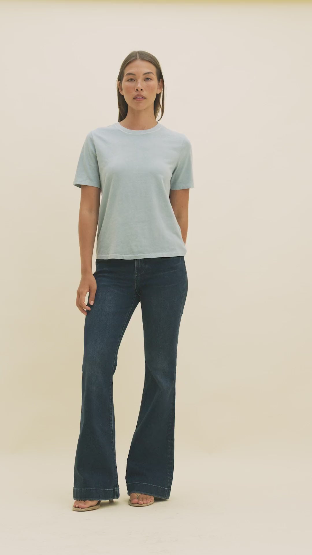 Video of a woman wearing dark flared jeans and a light blue t-shirt