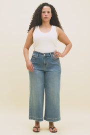 Video of a woman wearing a white tank top and medium blue ankle length wide leg jeans.