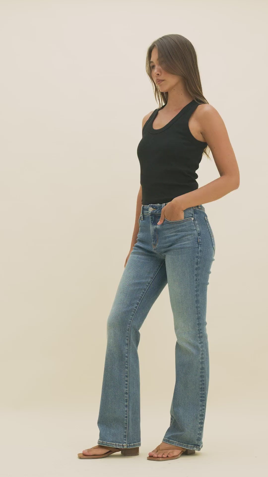Video of a woman wearing medium wash bootcut jeans and a black tank top