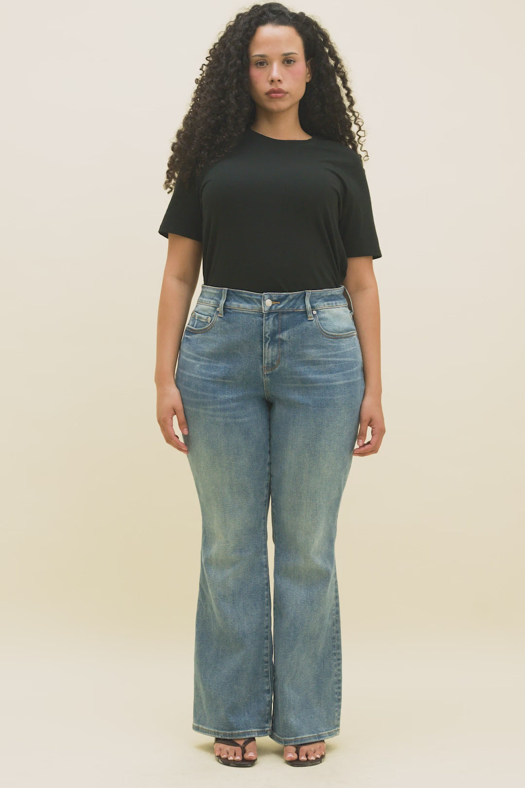 Video of a woman wearing a black crew t-shirt and medium blue boot cut jeans.