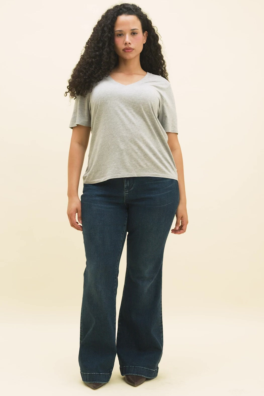 Video of a woman wearing a heather grey v-neck t-shirt and dark blue flare jeans.